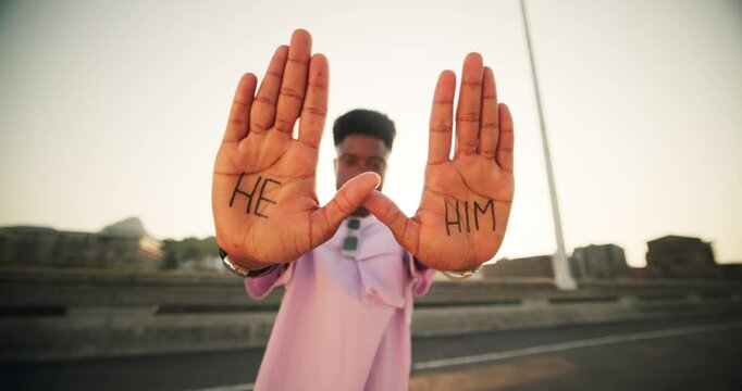 Man, face and hands with pronouns in city for gender identity, terminology and awareness. Male person, serious and smile with word text on palm at sunset for he, him and information on preference