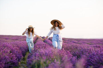 Happy mother with kid girl daughter running in blooming lavender field with flowers in field. Happiness. Springtime.