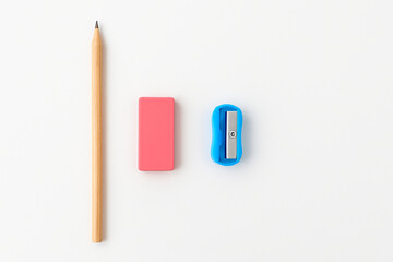  A wooden pencil, pink eraser, and blue sharpener arranged neatly on a white background, ideal for educational or school-related visuals.