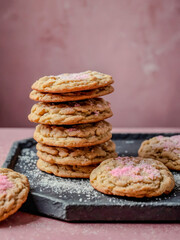 Pfeffernusse cookies stacked neatly on a slate plate, paired with a soft pink background and a light dusting of sugar.
