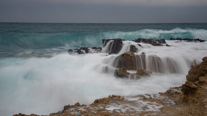 Turquoise waves crashing on rocks during stormy weather creating waterfalls