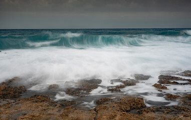 Turquoise ocean waves crashing on rocky coastline under dramatic sky