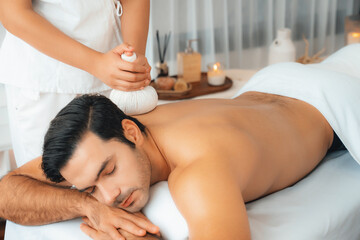 Hot herbal ball spa massage body treatment, masseur gently compresses herb bag on man body....