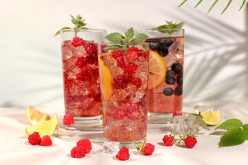 Modern still life with berry juice, raspberries, blueberries, red currants and oranges on elegant kitchen table with long hard shadows. Minimal detox diet concept, summer vitamin drinks