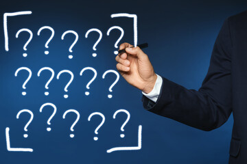 Businessman writing question mark on virtual screen against dark blue background, closeup