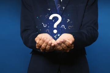 Businessman holding virtual question marks on dark blue background, closeup