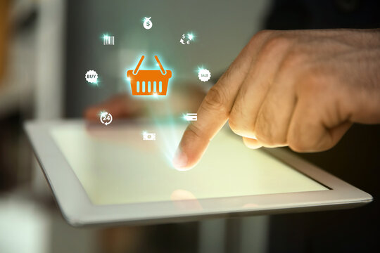 Online store. Man using tablet on blurred background, closeup. Illustration of shopping basket and other icons over device