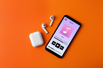 Mobile phone with open music player app, earphones and case on dark orange background, top view