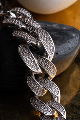 Close-up of luxury silver chain bracelet with crystal detailing on black stone and gold-toned background, professional jewelry photography for product branding, accessory catalog, fashion visuals