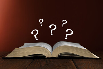 Question marks over open book on wooden table against brown background