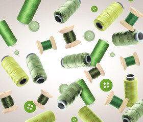 Many sewing threads and buttons in different shades of green flying on gradient background