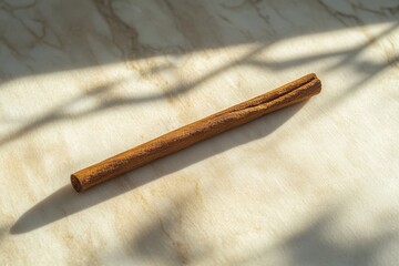 A single cinnamon stick lies on a light colored surface