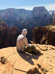 Male hiker sits on cliff edge overlooking stunning view of Zion canyon from West Rim Trail