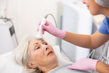Relaxed aged woman having face laser therapy by means of apparatus for aesthetic procedures used by...