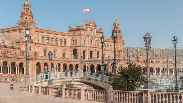 Plaza de Espana in Seville timelapse hyperlapse, a grand architectural complex in Maria Luisa Park built for the Ibero-American Exposition. Bridges, canal and vintage streetlights under blue sky.