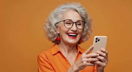 A smiling elderly woman with curly gray hair holds her smartphone, enjoying a moment of laughter. She wears stylish glasses and bold red earrings, set against a vibrant orange background.
