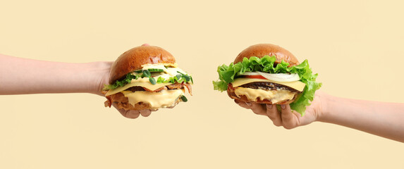 Female hands with tasty burgers on light yellow background
