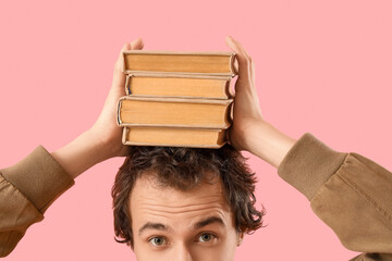 Young man with stack of books on pink background, closeup