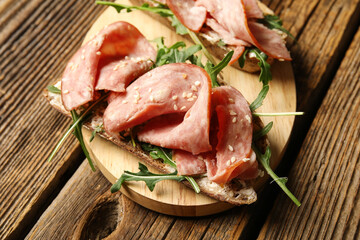Board of tasty bruschettas with ham on wooden background, closeup