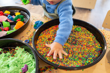 A tray filled with colorful sprinkles or rice, designed for sensory play activities where toddlers...