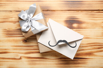 Envelope with paper mustache and gifts on wooden background. Father's Day celebration