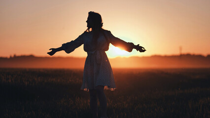 Woman silhouetted, arms spread wide, embracing golden wheat field sunset with joyful sense of...
