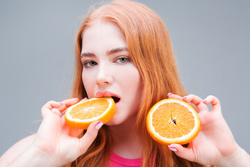 Young beautiful woman holding juicy halves of an orange in her hands isolated on gray background....