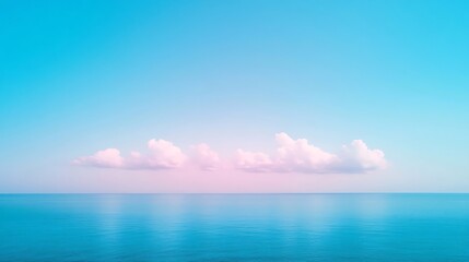 Obraz premium Serene expanse of blue ocean meets a calm pastel sky punctuated by soft fluffy clouds on the horizon.