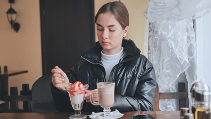 Female enjoying creamy dessert and cappuccino while seated at cozy cafe table