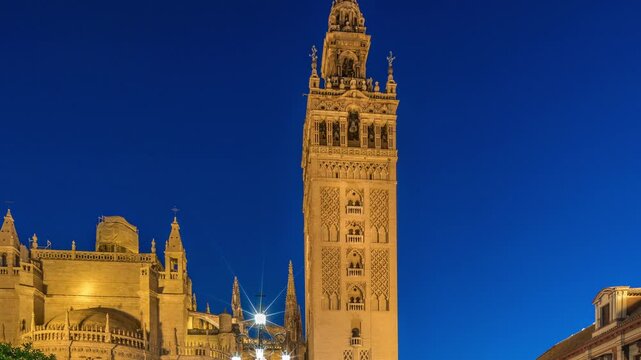 La Giralda and Seville Cathedral day to night transition timelapse, glowing with golden lights after sunset. The historic bell tower, gothic details and illuminated streets in Seville, Spain
