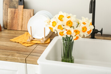 Vase with blooming narcissus flowers in sink, closeup
