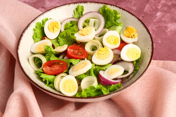 Tasty salad with quail eggs, tomatoes, onion and lettuce on pink background, closeup