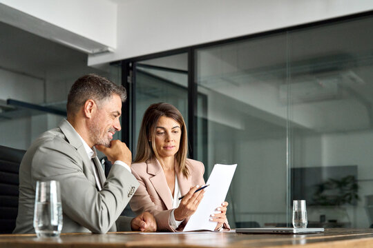 Two professional executives discussing financial accounting papers working with paperwork in office. Mature business woman and man managers holding legal corporate documents at meeting. Copy space.