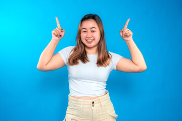 Happy young woman smiling and pointing up with both hands. Cheerful and positive facial expression,...