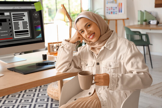 Muslim interior designer with cup sitting at table in office