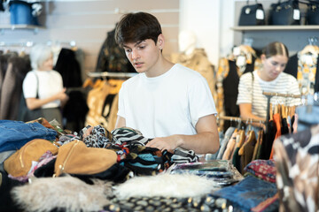 Guy buyer carefully sort through various wardrobe items presented in window of second-hand store, affordable and cheap clothes. Used goods store, stock season.