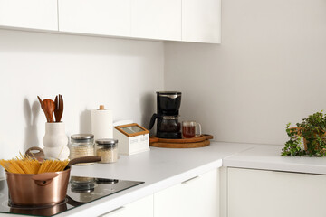 White counters with electric stove, cooking pot and utensils in modern kitchen