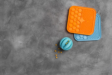 Ball for dog treats and dog licking mat on gray concrete background. Different pet accessories for...
