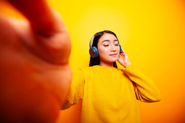 Asian vlogger standing against isolated backdrop and listening to music. Young woman with...