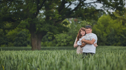 Obraz premium Happy family enjoying time together in nature, embracing their newborn baby in a serene green field beneath a majestic tree