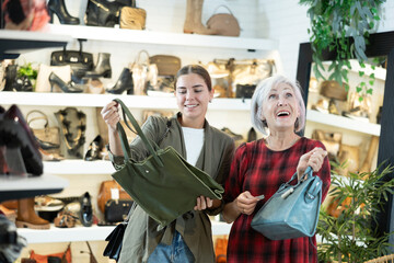 Mature woman with young daughter in store eye windowshopping product she likes and tactilely checks authenticity and naturalness of leather material from which bag is made.
