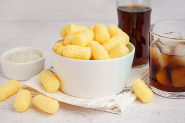 Bowl with tasty salty corn sticks, glass of cola and sauce on light background, closeup