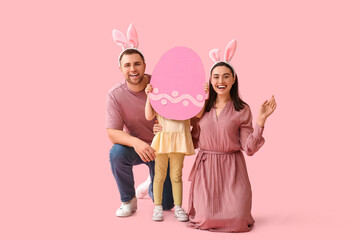 Happy family in bunny ears holding paper Easter egg on pink background
