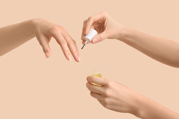 Female hands with bottle of cuticle oil on beige background