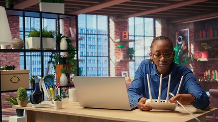 Black woman at home examines the modem and troubleshooting guide book, struggling to fix Wi Fi...