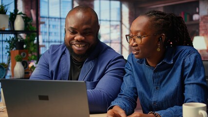 Black man and woman participating at a webinar remotely from home, listening to the online course with ear buds on laptop. Young couple freelancers using digital tools to develop their skills. Camera
