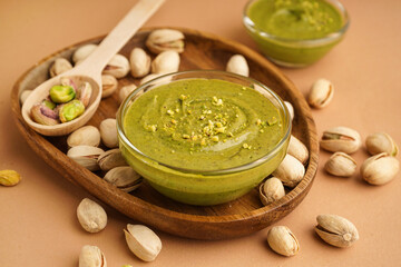 Wooden tray, spoon and bowl with pistachio paste on brown background