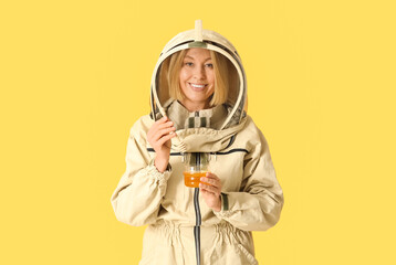Female beekeeper with jar of sweet honey and dipper on yellow background