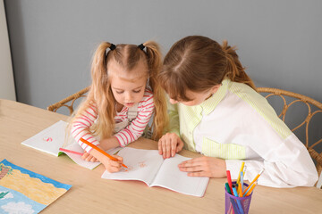Nanny with cute little girl drawing on table at home