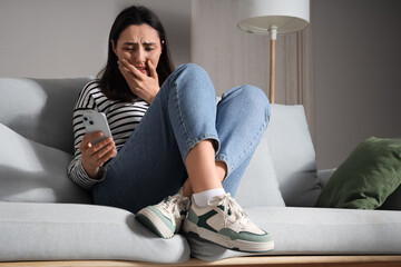 Depressed young woman using mobile phone on sofa at home